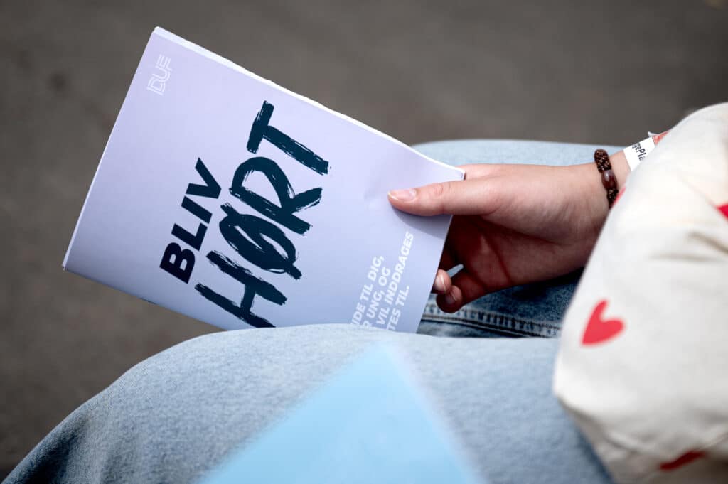 Hånd der holder DUFs publikation "Bliv Hørt"